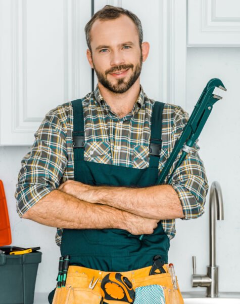 handsome plumber holding monkey wrench and looking at camera in kitchen